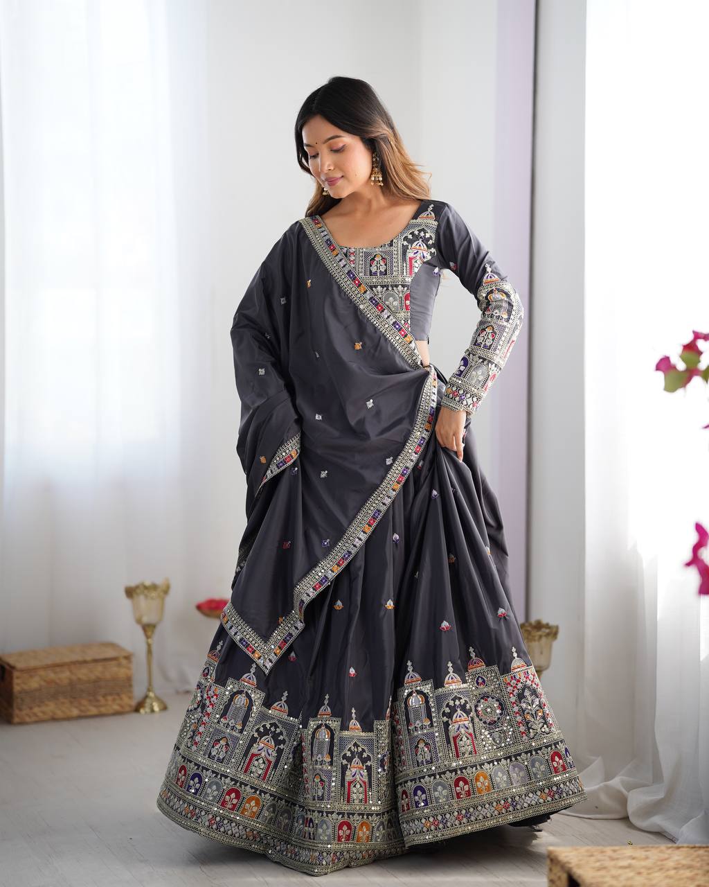 Woman wearing a dark grey  lehenga with intricate patterns in a minimalistic setting